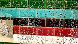 Droplets of water on a glass shower screen with colorful horizontal subway tiles in the background.