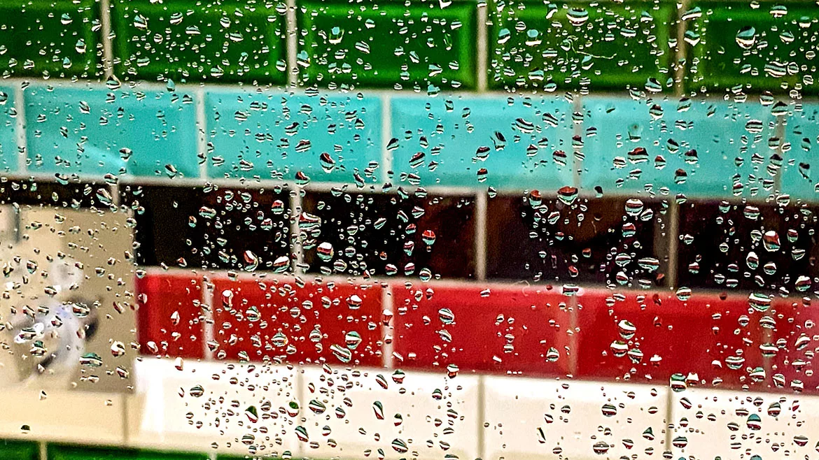 Droplets of water on a glass shower screen with colorful horizontal subway tiles in the background.