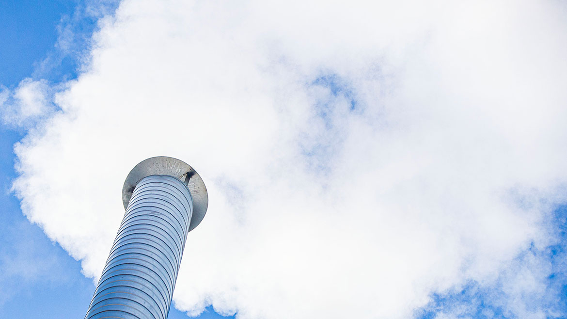 Metal chimney of a geothermal power station with stainless steel pipe structure with smoke and steam.