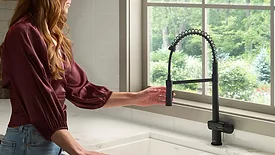 A woman using one of the new Ruvati faucets in a kitchen. 