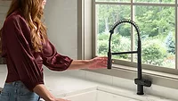 A woman using one of the new Ruvati faucets in a kitchen. 