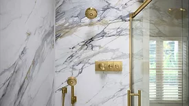 A shower with white marble and gold accessories. 
