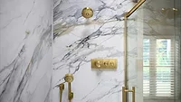 A shower with white marble and gold accessories. 