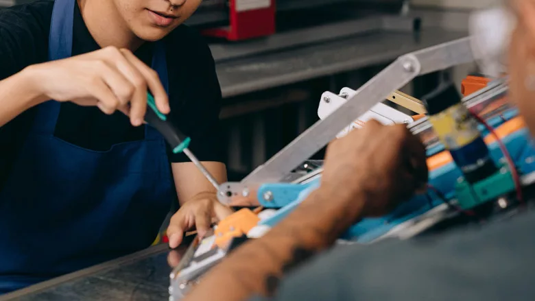 A young technician's hands working on a project while an older technician helps. 