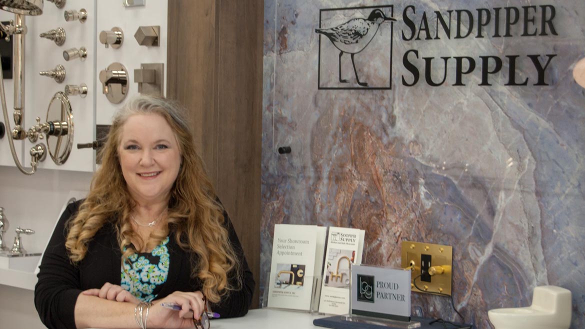 Sandpiper Supply Remodel feature image of Christy Ellis, showroom director, standing next to sign and brochures.