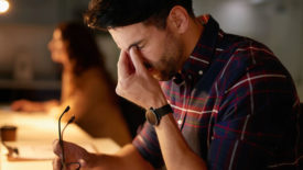 March 2024 Eye on Safety column feature image of stressed man holding glasses and rubbing his eyes with a blurred image of a woman in the background.