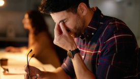 March 2024 Eye on Safety column feature image of stressed man holding glasses and rubbing his eyes with a blurred image of a woman in the background.