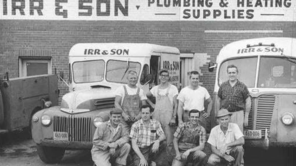 Black and white Irr & Son group photo of a eight men in front of two service vehicles
