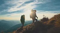 Two hikers climbing a mountain Two hikers in shadow climbing a mountain with the sun behind them.