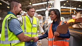 Three workers in safety vests meeting, two shaking hands.