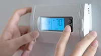 Hand adjusting thermostat on the wall.