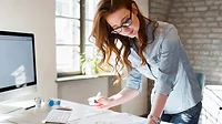 Woman standing by her desk with desktop computer, working
