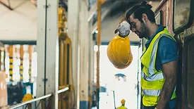 Worker leaning, wiping sweat off forehead, holding his safety hat in his hands.