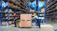 Workers moving stock in a warehouse with lettered blue shelves packed with packages in the background.
