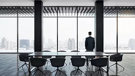 Businessman in front of an empty conference table, looking out of the window.