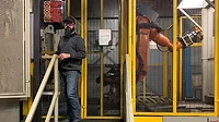 Employee at NIBCO standing by cobot in cage
