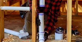 Plumber installing primer and glue PVC pipe at construction home.