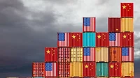 Cargo containers marked with US and Chinese flags, a cloudy gray sky in the background. 