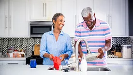Senior black couple doing dishes in the kitchen and smiling.