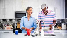 Senior black couple doing dishes in the kitchen and smiling.