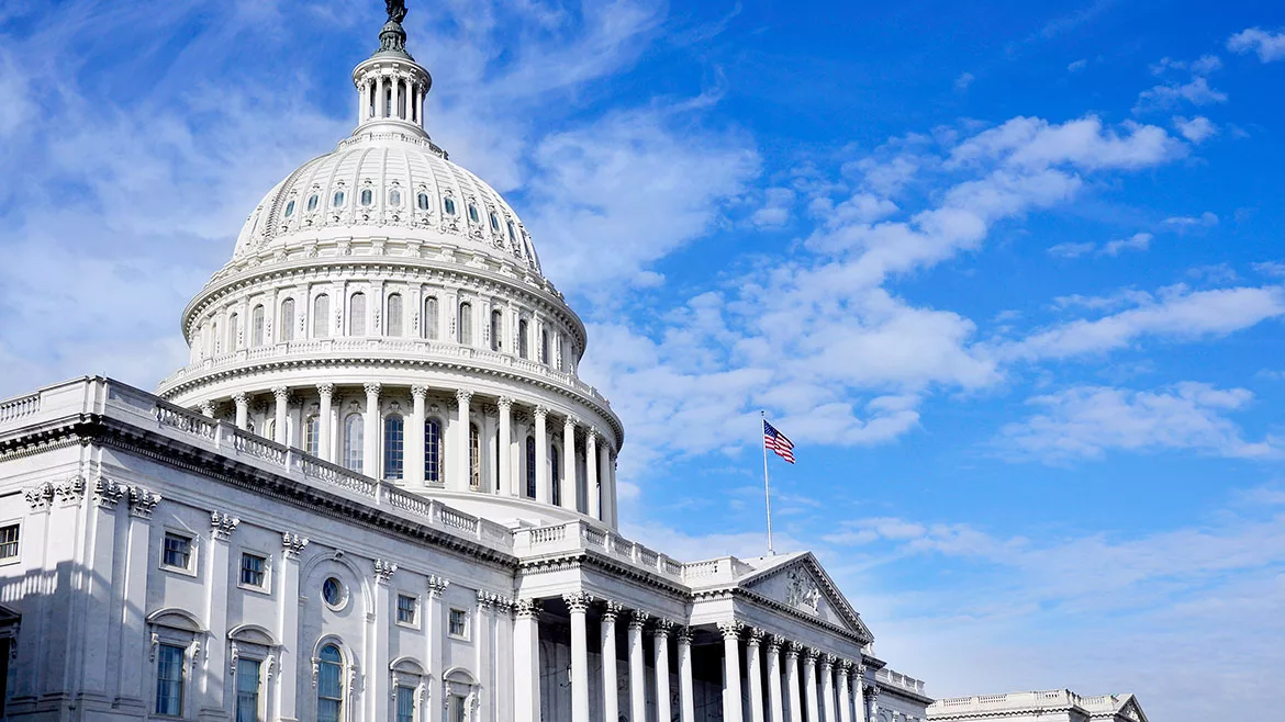 State Capitol in Washington D.C., a flag and cloudy blue sky in the background.