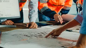 Closeup of a team of industrial engineers meeting to analyze machinery blueprints and consult on a project on a table in a manufacturing factory.