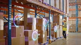 Retail warehouse worker in a safety vest and hard hat, scans inventory using a barcode scanner. A virtual infographics is displayed on the boxes.