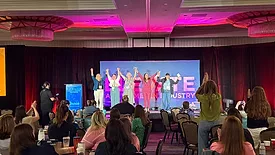 Women on the stage holding raised hands at ELEVATE Women in Industry. The audience are applauding.