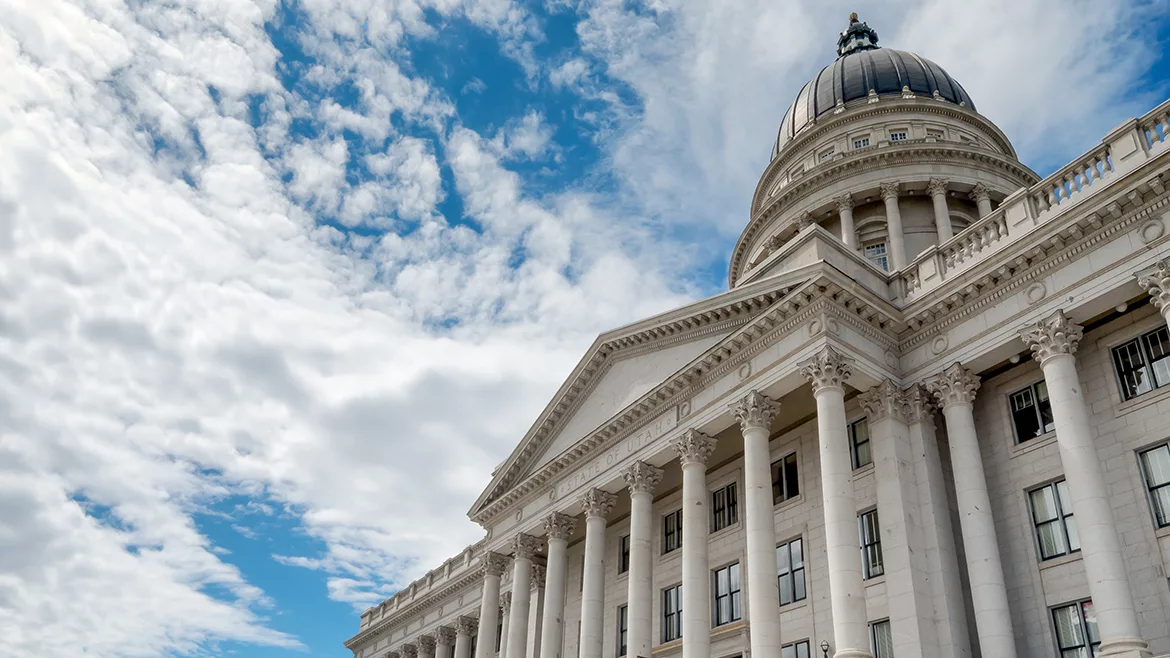 A cropped view of the United States Capitol building in Washington, DC with a cloudy blue sky in the background.