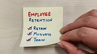 A sticky note on a wall with writing: EMPLOYEE RETENTION, three words each with a checked box - Retain, Motivate, Train