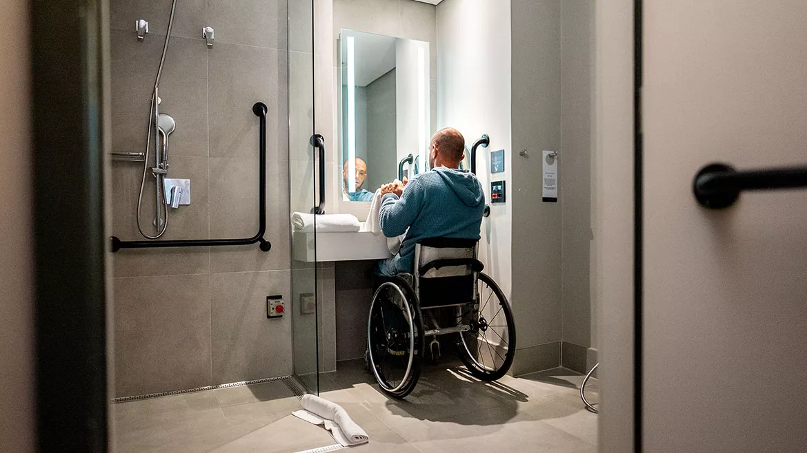 Mature man in a wheelchair drying his hands in the bathroom.