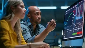 A woman and a man looking a computer screen with graphs, trading and charts.