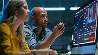 A woman and a man looking a computer screen with graphs, trading and charts.