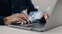 Person on a laptop with virtual graphs and charts floating above the keyboard.