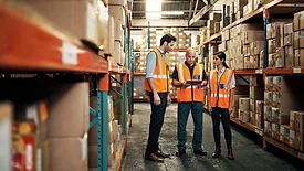 Warehouse employees talking, one holding a tablet for logistics, shipping and distribution.