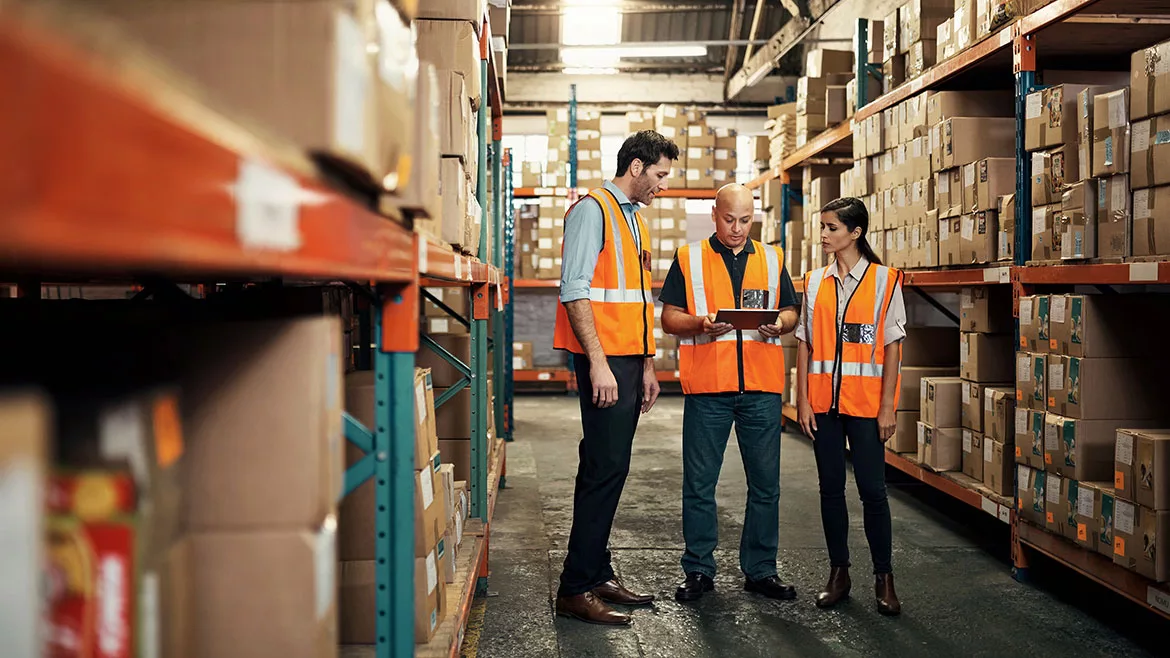 Warehouse employees talking, one holding a tablet for logistics, shipping and distribution.
