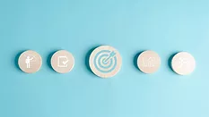 Round wooden blocks with business target objective icons on a light blue background.