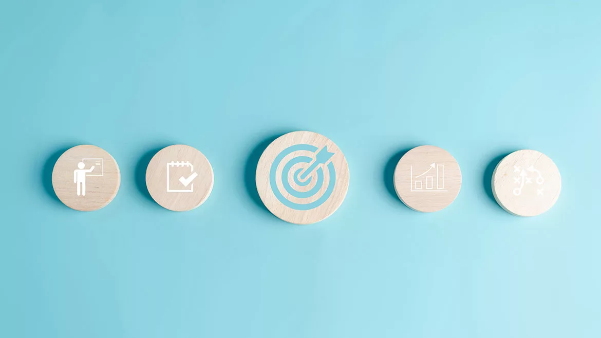 Round wooden blocks with business target objective icons on a light blue background.