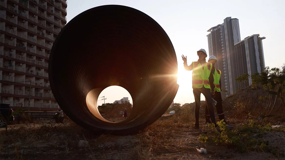 Two maintenance workers inspecting a large pipe for a water drainage project under construction.