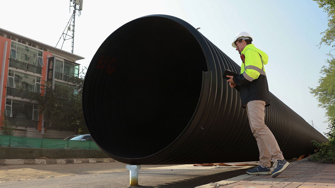 An engineer next to a giant sewage pipe at a construction site using a handheld equipment.