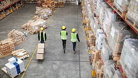 Workers working in large warehouse. Man moving boxed in a trolley with tow colleagues walking by in a distribution warehouse.