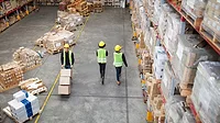 Workers working in large warehouse. Man moving boxed in a trolley with tow colleagues walking by in a distribution warehouse.