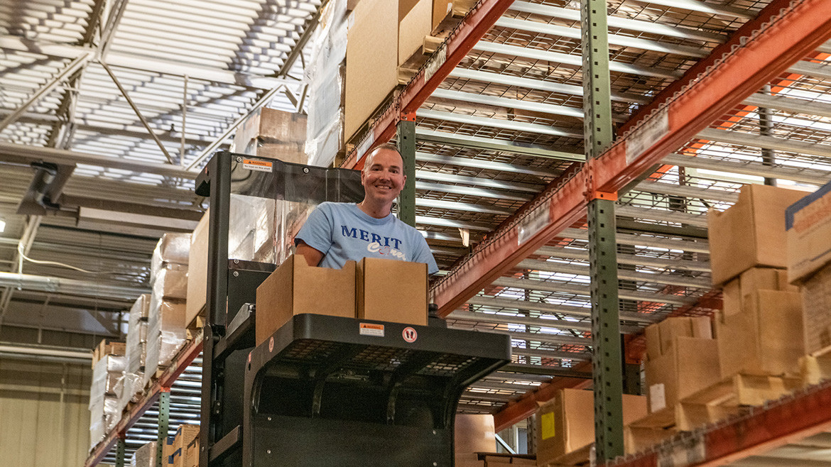Warehouse person on a forklift in a warehouse with tall shelves of boxes.