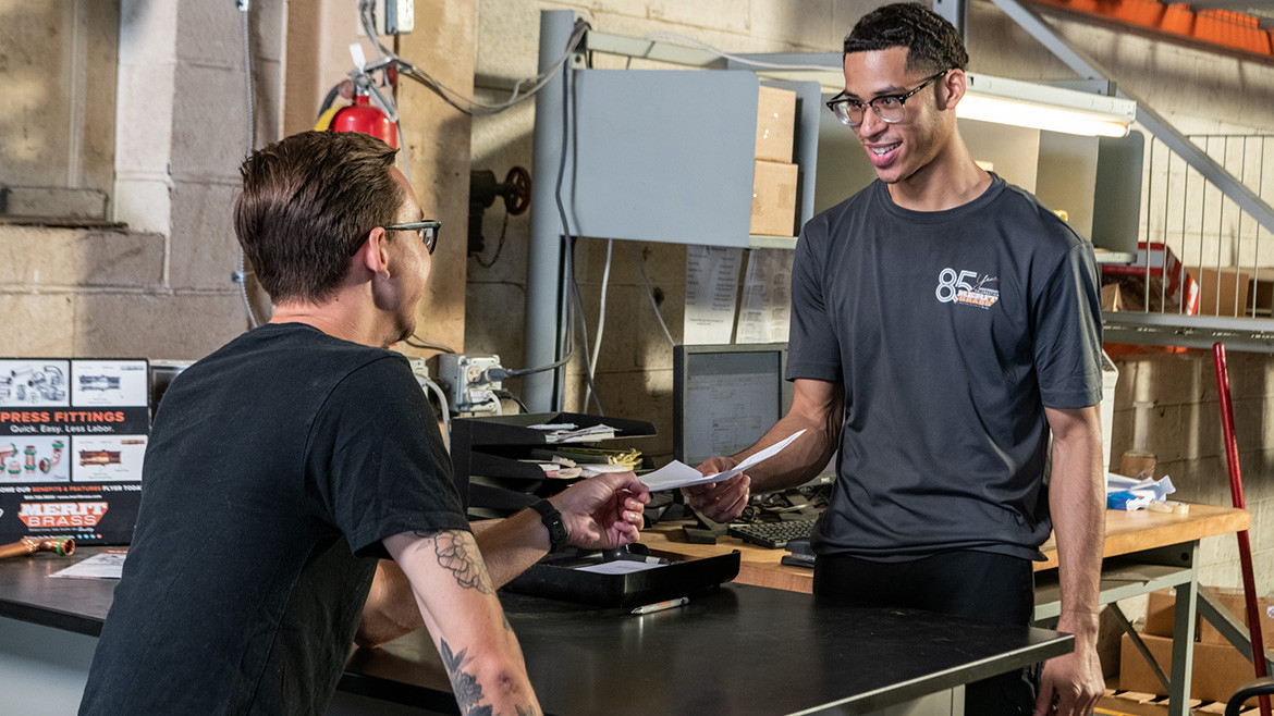 Will-call personnel handing over a piece of paper at a counter in a workshop or warehouse