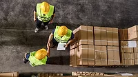 High angle view of two workers shaking hands while working with their colleague in distribution warehouse.