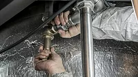 Plumber's hands gripping pipes to turn Plumber's hands with dirty sleeves, gripping pipes to turn it, a silver thermal material in the background.